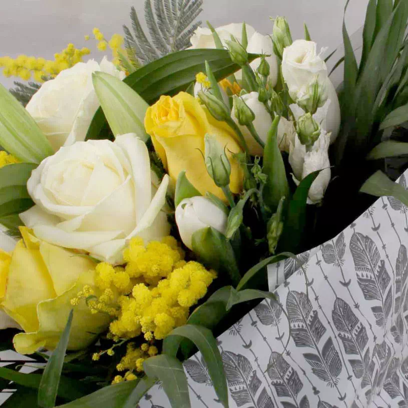 bouquet de fleurs jaunes et blanches emballé dans du papier cadeau blanc à imprimé plumes grises.